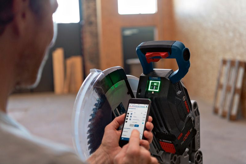 한 사람이 스마트폰 앱을 사용하여 무선 각도절단기를 조정하고 있습니다.