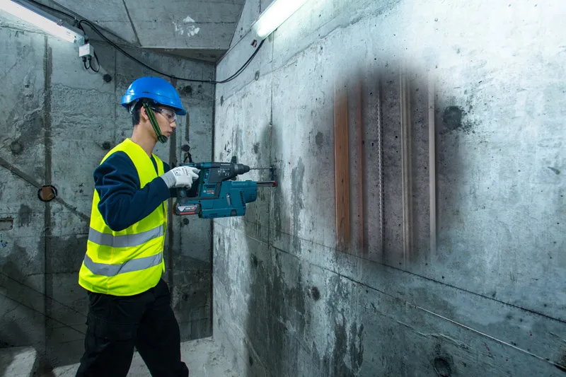 안전 장비를 착용한 사람이 탐지기로 콘크리트 벽을 검사해 내부에 파이프가 있는 것을 발견했습니다.