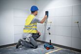 안전 장비를 착용한 사람이 타일 벽에 벽 스캐너를 사용하고 있습니다.