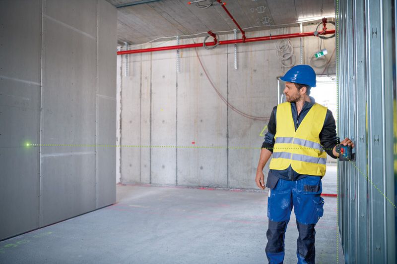 안전 장비를 착용한 사람이 레이저 레벨링 도구를 사용하여 벽 프레임을 정렬하고 있습니다.