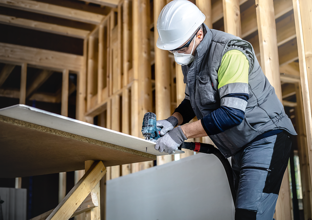 안전 장비를 착용한 사람이 전동 공구를 사용하여 나무 판자를 자르고 있습니다.