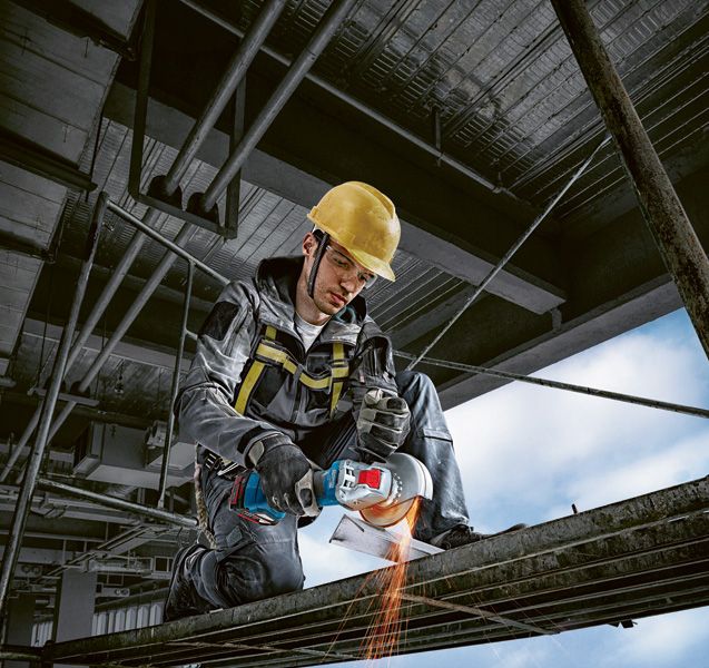 안전 장비를 착용한 사람이 각도 분쇄기를 사용하여 금속 빔을 자릅니다.