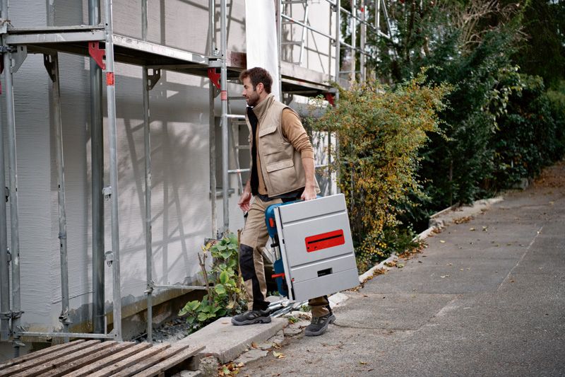 안전 장비를 착용한 사람이 건설 현장에서 무선 원형 톱을 운반하고 있습니다.