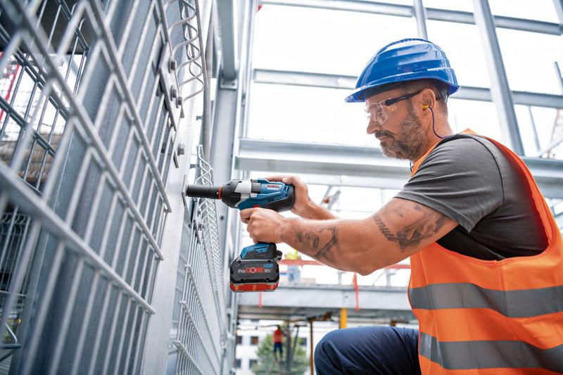 안전 장비를 착용한 사람이 무선 충격 렌치를 사용하여 금속 울타리를 작업하고 있습니다.