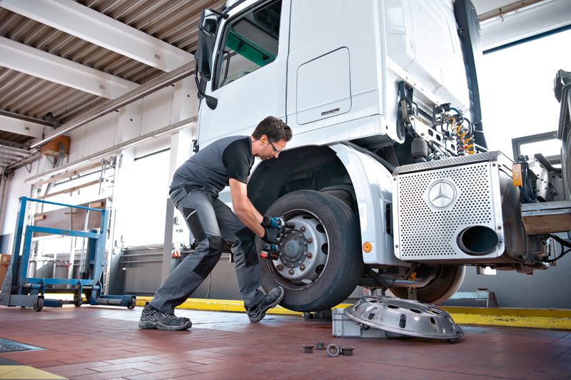 안전 장비를 착용한 사람이 충격 렌치를 사용하여 트럭 바퀴에서 볼트를 제거하고 있습니다.