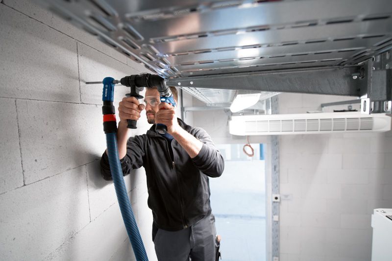 안전 장비를 착용한 사람이 FlexiClick 어댑터를 사용하여 콘크리트 벽에 구멍을 뚫고 있습니다.