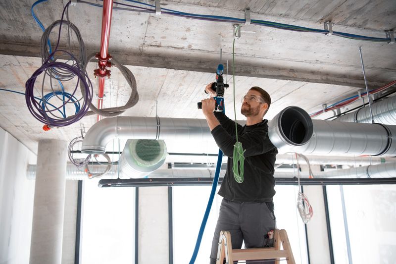 안전 장비를 착용한 사람이 사다리 위에서 FlexiClick 어댑터가 장착된 드릴을 사용하고 있습니다.