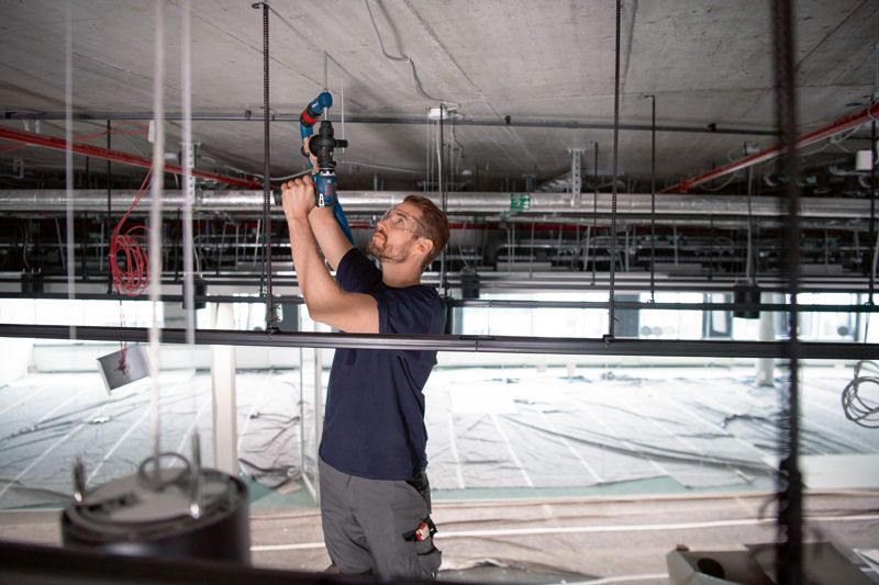 안전 장비를 착용한 사람이 FlexiClick 어댑터가 달린 드릴을 사용해 천장에 구멍을 뚫습니다.