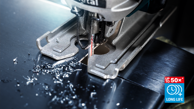 금속판을 자르는 직소톱날의 모습. 표면에는 금속 부스러기가 흩어져 있다.