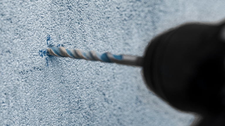 질감이 있는 콘크리트 벽에 구멍을 뚫는 드릴입니다.