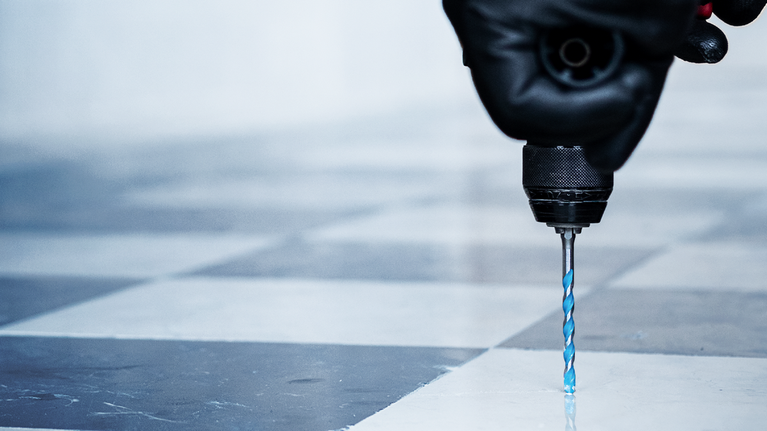 안전장비를 착용한 사람이 타일 바닥에 드릴을 박고 있습니다.