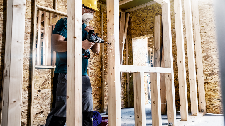 EXPERT Self Cut Speed 스페이드 드릴 비트 세트 14/16/18/20/22/24mm 6피스 안전 장비를 착용한 사람이 건설 현장에서 나무 프레임에 드릴을 박고 있다.