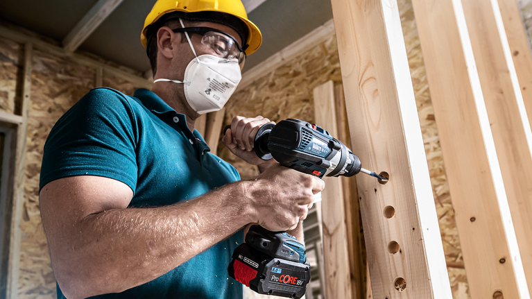 EXPERT Self Cut Speed 스페이드 드릴 비트 세트 14/16/18/20/22/24mm 6피스 안전장비를 착용한 사람이 나무 들보에 구멍을 뚫고 있습니다.