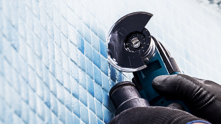 안전 장비를 착용한 사람이 휴대용 전동 공구를 사용하여 파란색 타일을 자르고 있습니다.