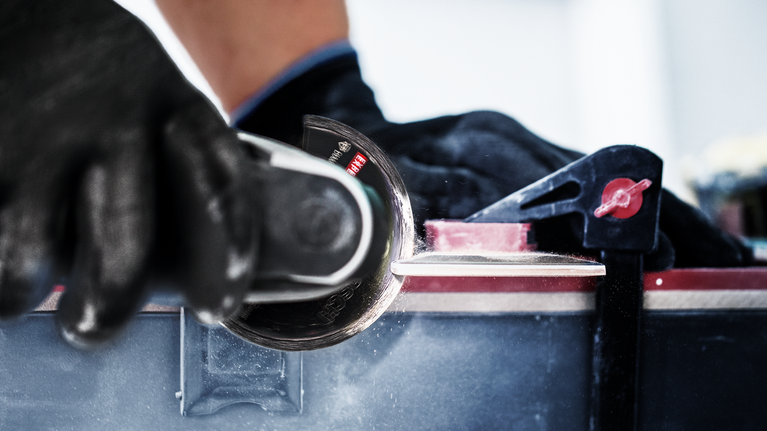 안전 장비를 착용한 사람이 작업대에 고정된 원형 톱으로 타일을 자르고 있습니다.