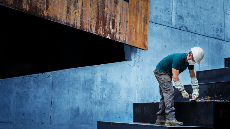 안전장비를 착용한 사람이 금속 계단에 구멍을 뚫고 있습니다.