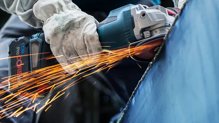 안전장비를 착용한 사람이 금속을 갈아서 밝은 불꽃을 낸다.