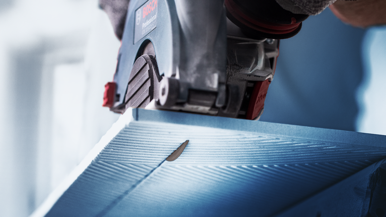 안전 장비를 착용한 사람이 원형 톱으로 파란색 패널을 자릅니다.