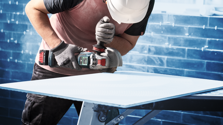 안전 장비를 착용한 사람이 작업대에서 시트 소재를 갈아내고 있습니다.