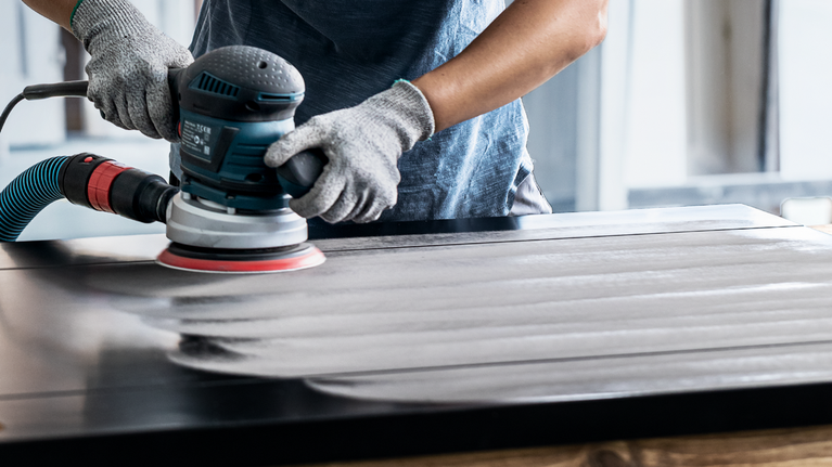 안전 장비를 착용한 사람이 전동 공구로 나무 표면을 연마하고 있습니다.