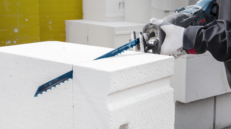 EXPERT ‘Aerated Concrete’ S 1241 HM 컷소날 1종 안전 장비를 착용한 사람이 왕복톱으로 흰색 콘크리트 블록을 자릅니다.