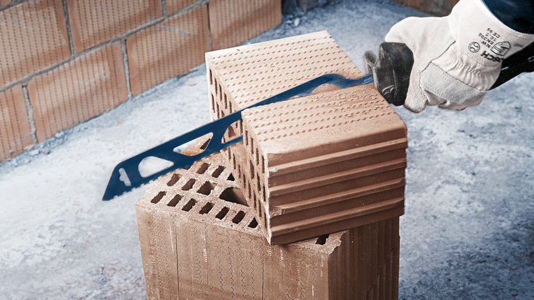 안전 장비를 착용한 사람이 손톱톱으로 벽돌 블록을 자릅니다.