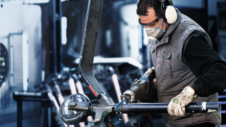 안전 장비를 착용한 사람이 산업 작업장에서 금속 파이프를 갈고 있습니다.