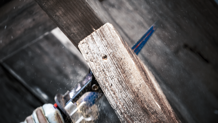 안전 장비를 착용한 사람이 왕복톱으로 나무 판자를 자릅니다.