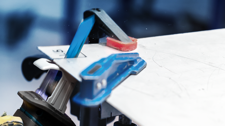 안전 장비를 착용한 사람이 작업대 위에서 전동 공구를 이용해 시트 소재를 자르고 있습니다.