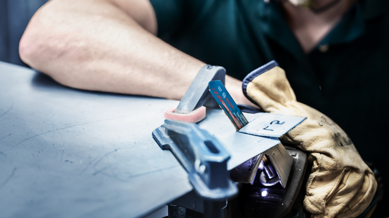 안전 장비를 착용한 사람이 장갑을 낀 손으로 금속판을 잡고 퍼즐을 사용하고 있습니다.