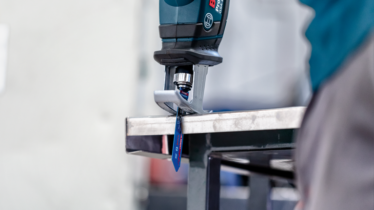 안전 장비를 착용한 사람이 왕복톱으로 금속판을 자릅니다.