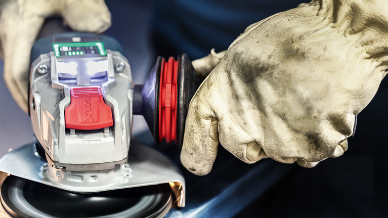 안전 장비를 착용한 사람이 금속 표면에서 각도 그라인더를 조작하고 있습니다.