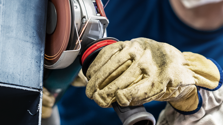 안전 장비를 착용한 사람이 회전 각도 분쇄기로 금속을 닦고 있습니다.