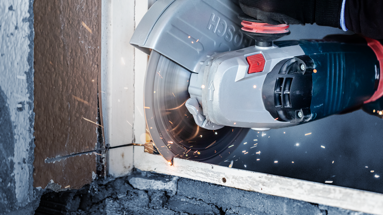 안전 장비를 착용한 사람이 대형 각도 그라인더로 금속 창틀을 자르고 있습니다.