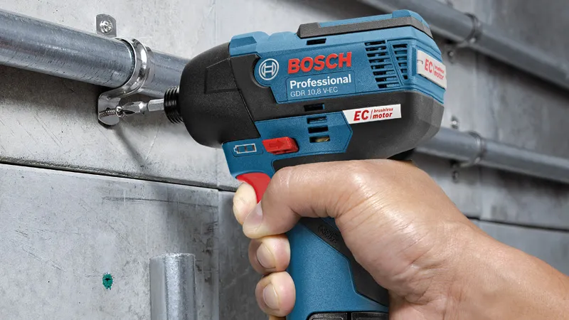 한 사람이 무선 충격 드라이버를 사용하여 콘크리트 벽에 금속 파이프를 고정하고 있습니다.
