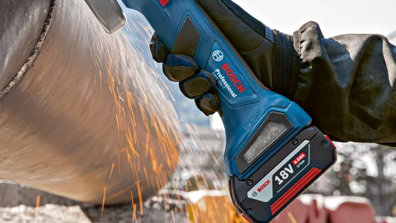 안전장비를 착용한 사람이 무선 각도 그라인더로 금속 파이프를 갈고 있습니다.