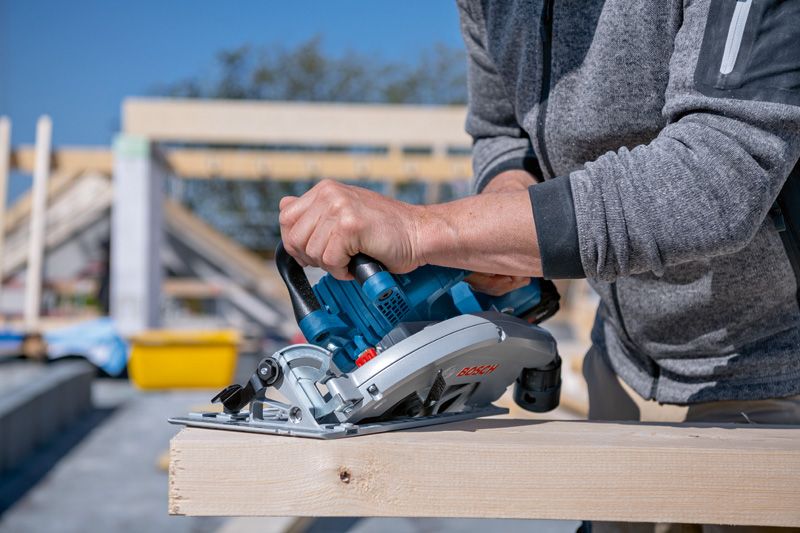 한 사람이 건설 현장에서 무선 원형톱을 사용하여 나무 판자를 자르고 있습니다.