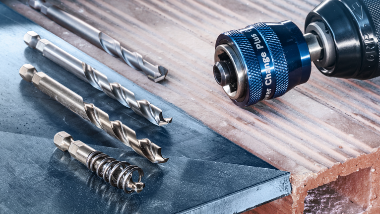 금속과 벽돌 표면에 여러 개의 드릴 비트를 놓은 드릴 드라이버입니다.