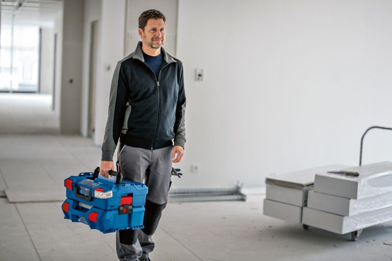 건설 현장에서 래치가 달린 파란색 적재형 운반 케이스 시스템을 들고 있는 사람.