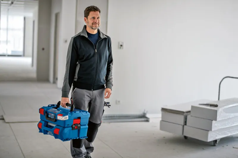 건설 현장에서 래치가 달린 파란색 적재형 운반 케이스 시스템을 들고 있는 사람.