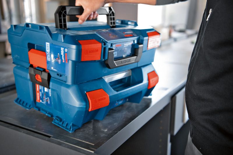 테이블 위에 주황색 래치가 달린 파란색 운반 케이스 시스템을 쌓아서 들어 올리는 사람.