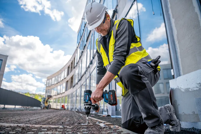 안전 장비를 착용한 사람이 건설 현장에서 무선 드릴 드라이버를 사용하고 있습니다.