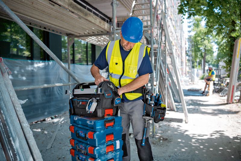 안전 장비를 착용한 사람이 건설 현장에서 쌓여 있는 도구 상자 위에 도구 가방을 정리하고 있습니다.