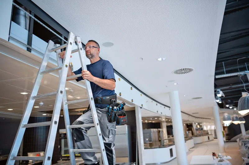 안전 장비를 착용한 사람이 사다리 위에 서서 도구 벨트 콤보 키트를 사용하고 있습니다.