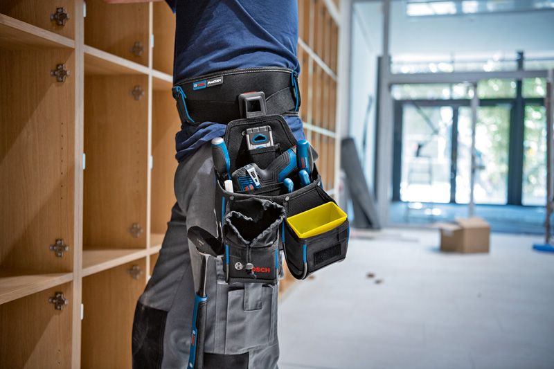 안전 장비를 착용한 사람이 측정 도구를 담은 도구 벨트를 이용해 선반을 설치하고 있습니다.