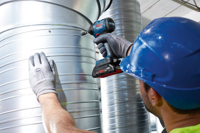 안전 장비를 착용한 사람이 무선 전동 드릴을 이용해 금속 덕트를 고정하고 있습니다.