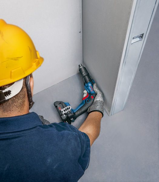 안전장비를 착용한 사람이 전동공구를 이용해 건식벽체에 나사를 박고 있습니다.