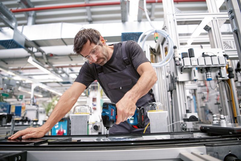 안전 장비를 착용한 사람이 산업 조립 라인에서 무선 드릴을 사용하고 있습니다.