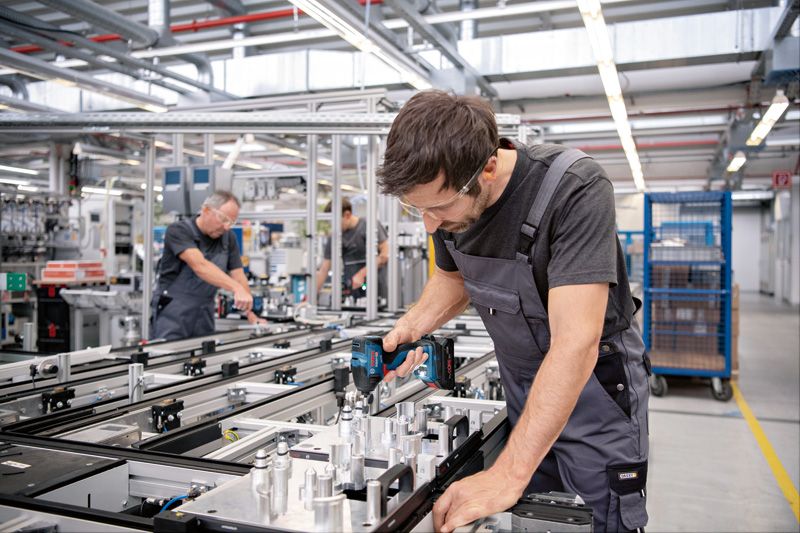 안전 장비를 착용한 사람이 조립 라인에서 무선 드릴을 사용하고 있습니다.