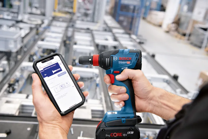 한 사람이 산업 현장에서 무선 드릴을 제어하기 위해 스마트폰을 사용하고 있습니다.